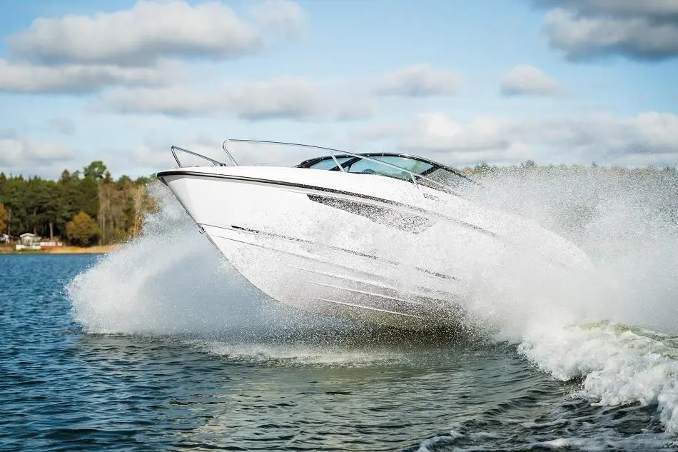 A sleek white motorboat jumps over water, creating a splash against a serene lake backdrop with trees and clouds.